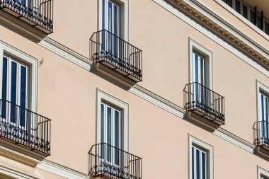 Valencia 'da modern bir bina cephesinin yakın plan görüntüsü karmaşık bir şekilde tasarlanmış balkonlar ve geniş pencereler berrak mavi gökyüzünün altında şeftali rengi bir duvara karşı..