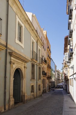 Alicante İspanya - 12 Temmuz 2025: Alicante 'de açık mavi gökyüzü altında geleneksel mimari ve canlı binaların sergilendiği güzel dar bir cadde.