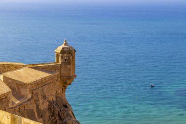 Castillo de Santa Barbara 'nın Alicante' deki sakin Akdeniz manzarası açık güneş ışığında tarihi mimari ve kıyı manzarasını gözler önüne seriyor..
