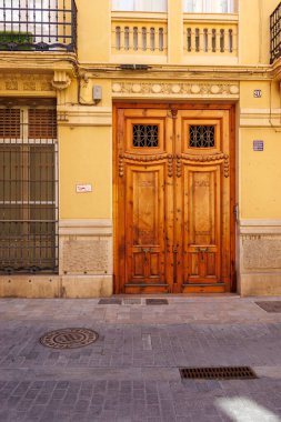 Valencia İspanya - 13 Temmuz 2025: Valensiya 'nın tarihi mahallesindeki sarı bir binanın ahşap kapıları geleneksel mimarlık ve işçilik sergileniyor.