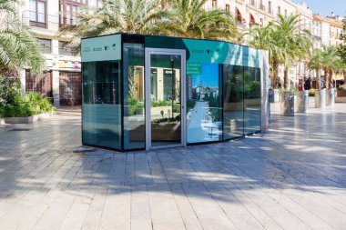 Valencia İspanya - 13 Temmuz 2025: Canlı bir şehir meydanında palmiye ağaçlarıyla çevrili modern cam büfe kentsel yaşamın ortasında bir turist bilgi servisini gözler önüne seriyor.