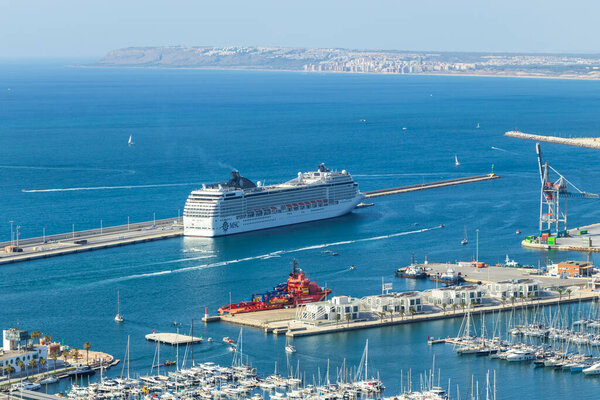 Аликанте Испания - 12 июля 2025: Круизное судно отходит от оживленного порта Аликанте в окружении небольших лодок и яхт, создающих оживленную морскую сцену.