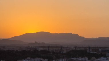 Alicante yakınlarındaki dağların üzerinde gün batımı canlı turuncu gökyüzüne karşı siluet şekilleri vurguluyor akşamın erken saatlerinde sakin bir atmosferi yakalıyor..
