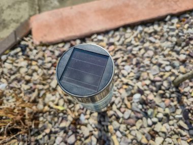 Çakıl taşlarının üzerine kurulmuş güneş enerjisiyle çalışan bahçe ışığının yakın plan çekiminde modern açık hava aydınlatma teknolojisi ve gündüz çevre dostu enerji kullanımı sergileniyor..
