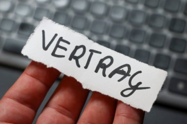 Üzerinde VERTRAG yazan bir kağıt parçasını tutan bir el. Arkaplanda iş ve sözleşme temaları çağrıştıran bulanık bir klavye yer alıyor.