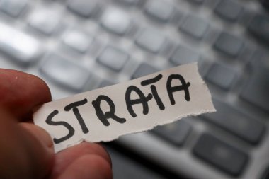 Modern hayatın kayıp bilgilerini ve dijital bağlamını sembolize eden dizüstü bilgisayarın arka planında STRATA sözcüğünü içeren yırtık bir kağıdı tutan bir el..