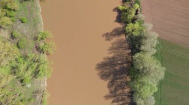 Kahverengi nehrin yukarıdan aşağıya havadan görünüşü ve baharda yeşil bitki örtüsü olan ekili alanlar, kırsal alan şekilleri.