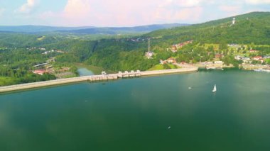 Solina Gölü ve barajın panoramik manzarası. Bir yelkenli ve canlı doğal çevresi var..