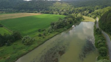 Yeşil tarlalardan akan kıvrımlı bir nehrin ve kırsal kesimdeki ağaçlık tepelerin havadan çekilmiş görüntüleri..