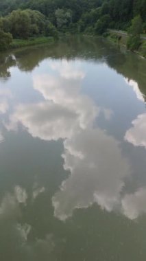 Durgun bir nehrin havadan çekilmiş görüntüsü gökyüzünü yansıtıyor, doğal bir manzaradaki yemyeşil bir ormanla çevrili..