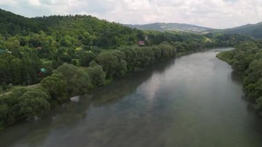 Yoğun ağaçlar ve tepelerle çevrili verimli bir vadiden akan dolambaçlı bir nehrin havadan görünüşü..