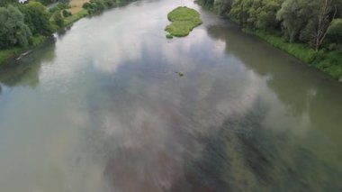 Yoğun yeşillik ve açık alanlarla çevrili küçük yeşil adalı bir nehrin havadan çekilmiş görüntüsü..