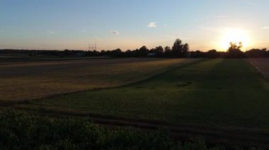 Gün batımında altın tarlaların havadan panoramik görüntüsü, sıcak güneş ışığı manzaranın üzerine uzun gölgeler düşürüyor..