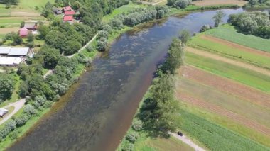 Yakınındaki evler ve tarlalarla bir nehir kıyısının insansız hava aracı görüntüsü kırsal bir araziyi vurguluyor..