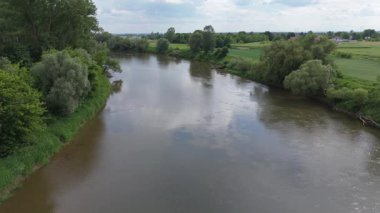 Sakin bir nehrin kayan bulutları yansıtan, yeşil ağaçlarla kaplı kıyıların altında yavaş hareket eden suyu yansıtan videosu..