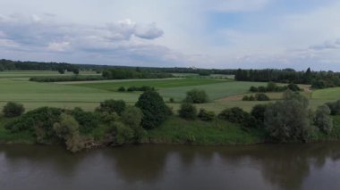 Yumuşak gün ışığı altında yeşil tarlalar ve çitlerle kaplı kıvrılan bir nehir kıyısı videosu..