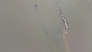 Batık ahşap direkleri ve yaz güneşi altında hafif dalgalanmaları olan sığ bir nehrin havadan çekilmiş videosu..