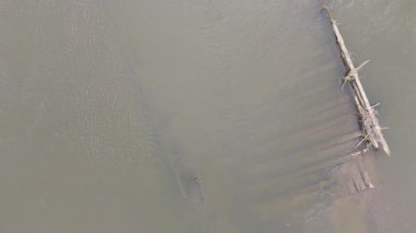 Eski batık ahşap direklerin, sığ nehir suyunda doğrusal dalgalanmalar yaratan havadan çekilmiş makro videosu..