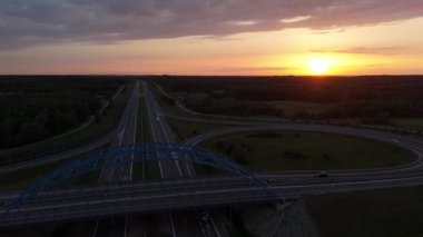 Üstgeçit köprüleriyle karayolu kavşağının hava günbatımı görüntüsü, renkli akşam gökyüzü altında hareket eden trafik.