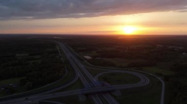 Otoyol ve kavşağın geniş hava günbatımı görüntüsü, ufuktan ufka yol bağlantı, seyahat ve hareketi simgeliyor..
