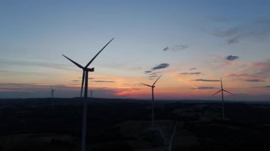 Günbatımında rüzgar çiftliğinin drone alacakaranlık görüntüsü, kırsal alanda sürdürülebilir temiz enerji üreten yenilenebilir türbinler.