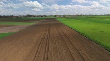 Bulutlu gökyüzü altında yeşil tarlaları olan çiftliklerin insansız hava aracı görüntüsü, kırsal ilkbahar tarım manzarası.