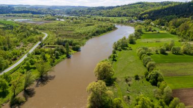 Parlak bir gökyüzünün altındaki yemyeşil ve tarım alanlarında süzülen manzaralı nehir manzarası bahar boyunca kırsal kesimde doğanın güzelliğini gözler önüne seriyor..