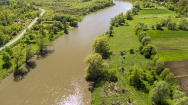 Baharda yemyeşil tarlalar ve ağaçlarla çevrili dolambaçlı bir nehrin havadan görünüşü. Sahne, çevre temaları için ideal doğanın güzelliğini yakalıyor..