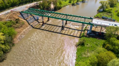 Modern yeşil bir köprünün inşaatı nehir mühendisliği alanında ilerleme kaydetti. Gündüzleri yemyeşil ile çevrelenen sahne gelişimi simgeler..