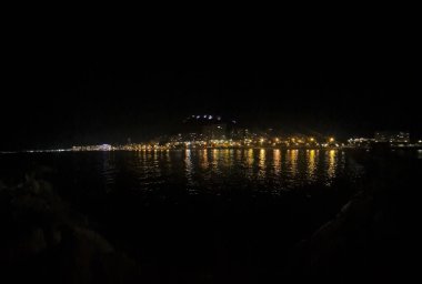Beautiful night view of Alicantes skyline reflecting in the calm ocean waters showcasing lively city lights. Perfect for travel magazines and promotional materials.