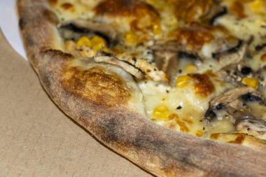 A close-up view of a delicious pizza showcasing golden cheese and toppings including mushrooms and corn served in a cardboard box emphasizing comfort food.