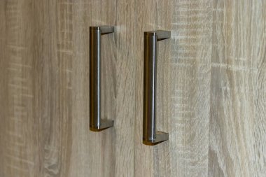 Ahşap bir kabine yüzeyine bağlı modern metalik sapların yakın görüntüsü ev dekorasyonlarında işlevsellik ve stil sağlar.