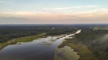 Gün batımında yemyeşil yemyeşil ile çevrili sakin bir nehir manzarası. Sakin su renkli gökyüzünü yansıtır doğada barışçıl bir atmosfer yaratır..