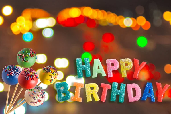Happy birthday greeting card, candy on sticks on a background with colorful bokeh