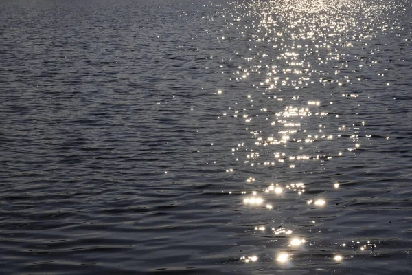 Image of a wavy water surface in which the sun is reflected in the form of a flickering light path