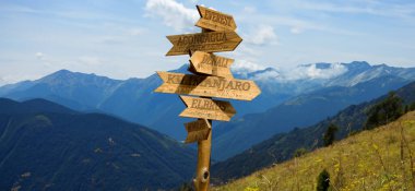 Dağların yüksekliğini ve uzaklıklarını gösteren dağların tepelerinin yönlerini gösteren tahta bir işaretçi resmi.