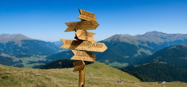 Dağların yüksekliğini ve uzaklıklarını gösteren dağların tepelerinin yönlerini gösteren tahta bir işaretçi resmi.