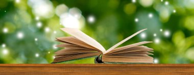 Ahşap bir yüzey üzerinde bir kitap yatar, sayfaları geniş bir zemin üzerinde yayılmış canlı yeşil yapraklar.