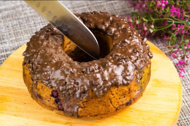 Zengin çikolata jöleli yeni pişmiş bir pasta ustalıkla dilimleniyor. Tahta kırsal bir dokunuş sağlıyor, canlı çiçekler ise ayara cazibe katıyor..