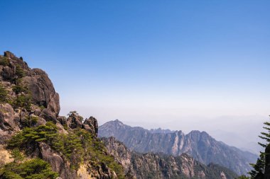 Çin 'deki görkemli dağların nefes kesici manzarası. Açık mavi gökyüzü ve engebeli tepeler çarpıcı bir manzara yaratır. Yürüyüşçüler ve doğa severler için mükemmel..