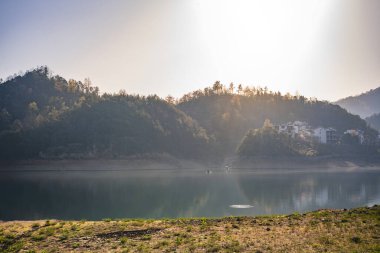 Yükselen dağların arasına kurulmuş bir göl üzerinde sakin ve sakin bir gün doğumu manzarası. Sis suyun üzerinde sallanıyor ve nefes kesici bir atmosfer yaratıyor. Dağların yansıması ve suyun üzerindeki yumuşak güneş ışığı güzel, huzurlu bir ışık yaratıyor. 