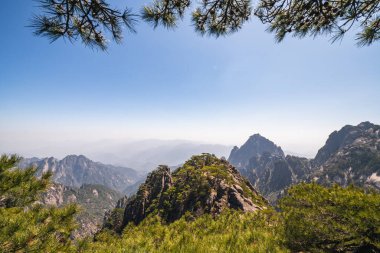 Çin 'deki Huangshan dağ sırasının nefes kesici panoramik manzarası. Bereketli yeşil ormanlar ve kayalık tepeler berrak mavi gökyüzüne yükseliyor. Uçsuz bucaksız vadi aşağıya doğru uzanır ve olağanüstü bir doğal manzara yaratır..