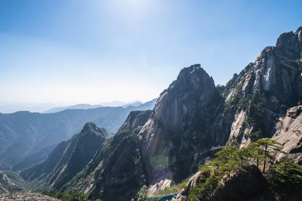 Çin 'deki görkemli Huangshan dağ sırasının nefes kesici panoramik manzarası. Engebeli tepeler, yemyeşil orman ve vadilerle çevrili gökyüzünü deler. Doğanın uçsuz bucaksız genişliğinde bir sükunet ve güzellik duygusu aşikardır. Trave için mükemmel.