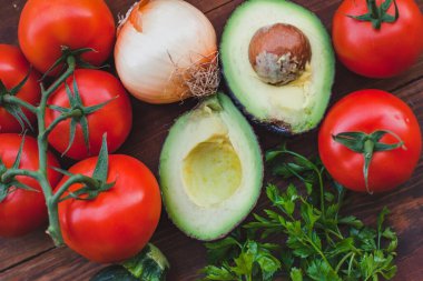 Domatesli avokado ve ahşap arka planda soğan, taze sebzeler.