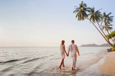 romantic young couple walking together on beautiful exotic tropical beach at sunset clipart