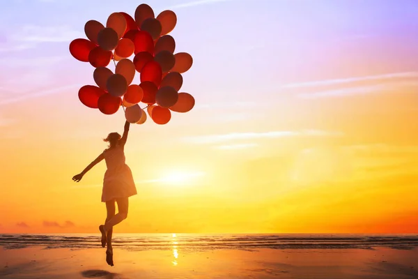 快乐或梦想的概念 一个快乐的女人在日落时分带着五彩缤纷的气球在海滩上跳跃的轮廓 — 图库照片