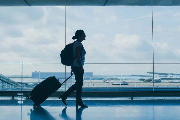 空港での出発スーツケースを持って歩く女性のシルエットコピースペースでの旅行の背景 — ストック写真