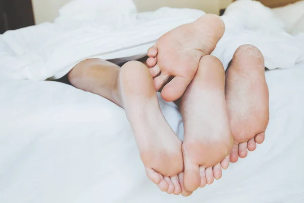 ホテルのベッドで毛布の下で寝てる夫婦の足 — ストック写真