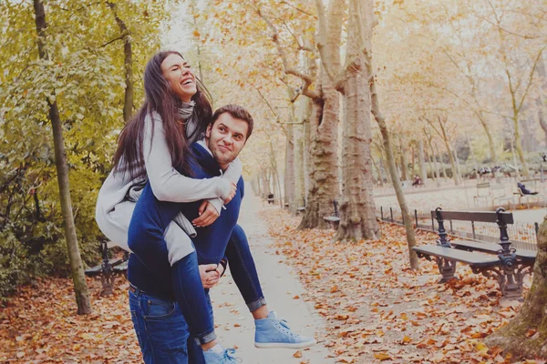 女性のピギーバックを運んでいる男日付秋の公園で笑っている若いカップル — ストック写真