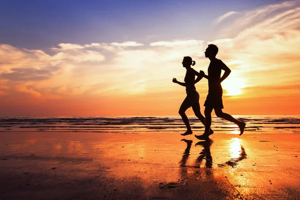 日没のビーチでジョギングをしている人のシルエットが — ストック写真